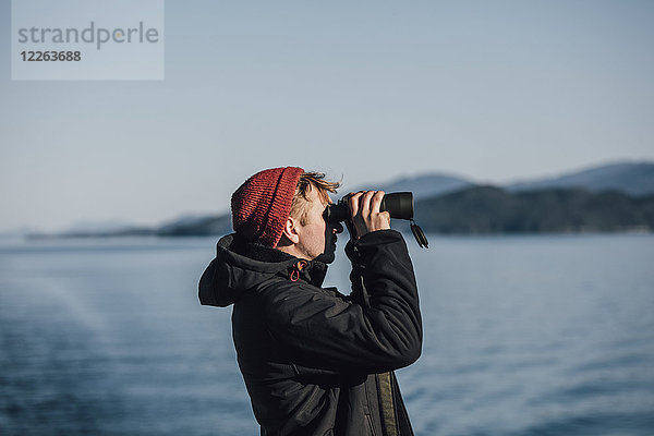 Kanada  Britisch-Kolumbien  Mann schaut durchs Fernglas an der Küste.