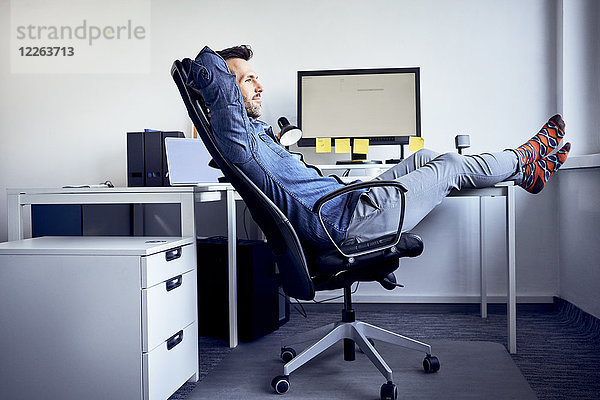 Mann sitzt am Schreibtisch und entspannt im Büro