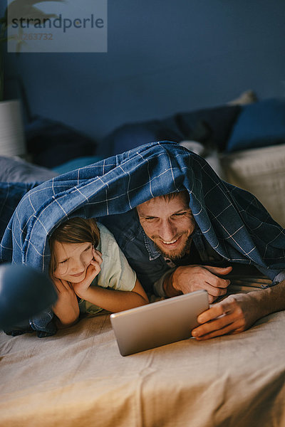 Glücklicher Vater und Sohn sehen sich einen Film unter der Decke an.