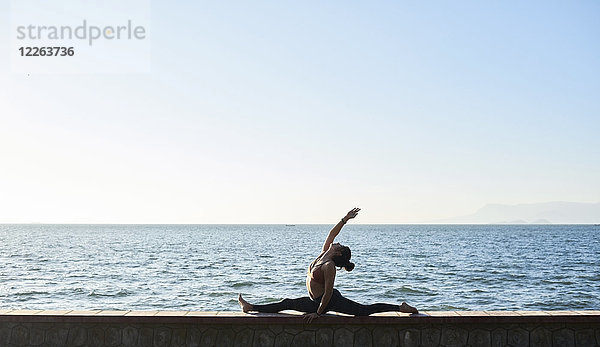 Junge Frau beim Yoga an einer Wand am Meer