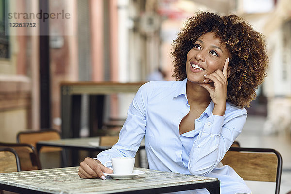 Lächelnde Frau mit Afro-Frisur sitzend im Outdoor-Café