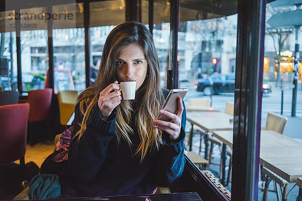 Paris  Frankreich  Portrait einer jungen Frau mit Smartphone  die in einem Café Espresso trinkt.