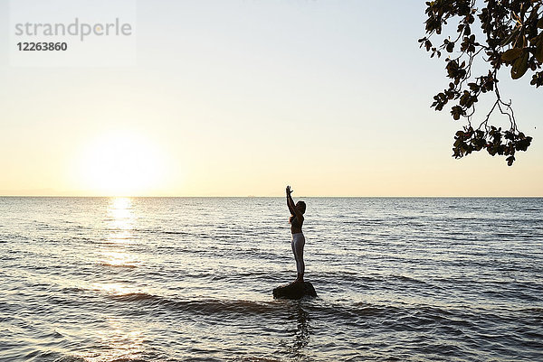 Junge Frau beim Yoga auf einem Felsen im Meer bei Sonnenuntergang