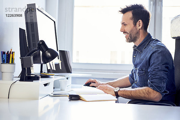 Lächelnder Mann bei der Arbeit am Computer am Schreibtisch im Büro