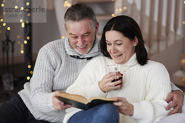 Glückliches reifes Paar beim Lesen eines Buches im Wohnzimmer