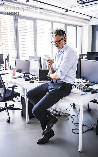 Reife Geschäftsleute sitzen auf dem Schreibtisch im Büro mit dem Smartphone