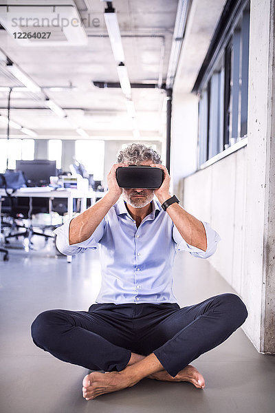 Barfuss reifer Geschäftsmann mit VR-Brille auf dem Boden im Büro sitzend