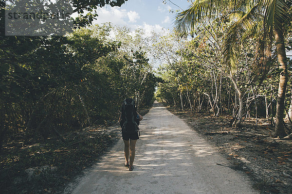 Kuba  Cienaga de Zapata  Junge Frau mit Rucksack  die auf einer von Bäumen gesäumten Straße läuft.