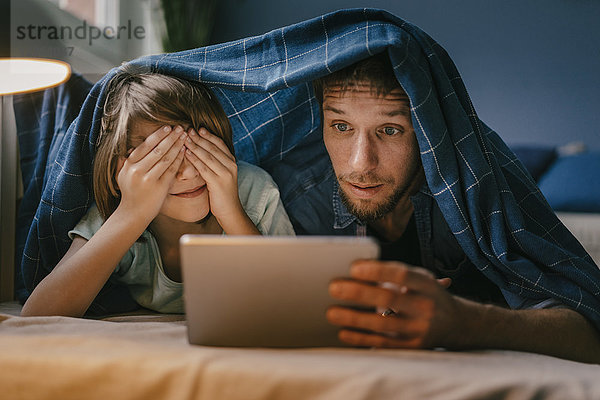 Aufgeregter Vater und Sohn beim Betrachten eines Films auf Tablett unter der Decke