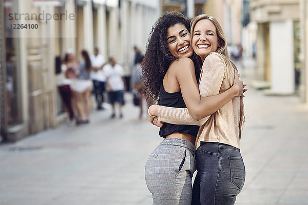 Porträt zweier glücklicher Freunde  die sich auf der Straße umarmen