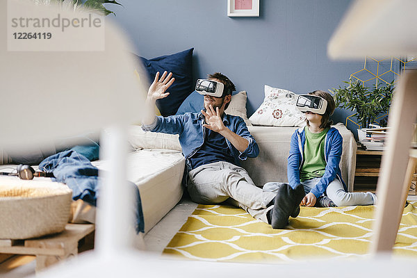 Vater und Sohn mit VR-Brille zu Hause auf dem Boden sitzend