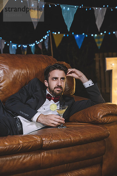 Nachdenklicher Mann im Anzug  der auf dem Sofa auf einer Nachtparty liegt.