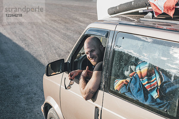Porträt eines glücklichen jungen Mannes mit einem Minivan auf einem Roadtrip