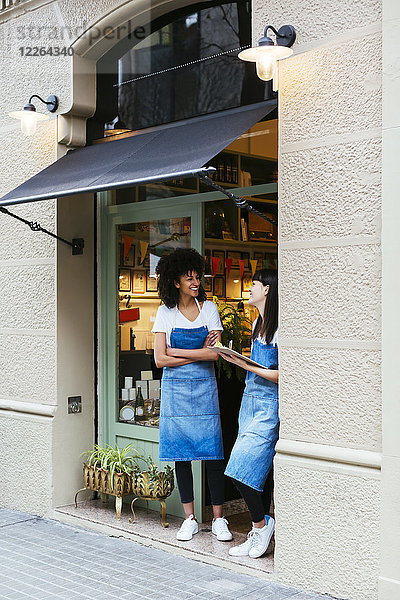 Zwei glückliche Frauen stehen in der Eingangstür eines Ladens.