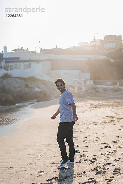 Glücklicher junger Mann  der bei Sonnenuntergang am Strand spazieren geht.