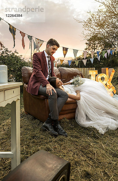 Braut auf dem Sofa liegend mit Bräutigam auf dem Feld
