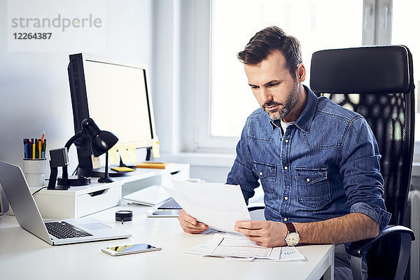 Mann liest Dokument am Schreibtisch im Büro