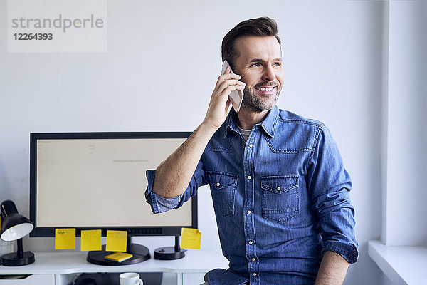 Lächelnder Mann am Schreibtisch im Büro beim Telefonieren