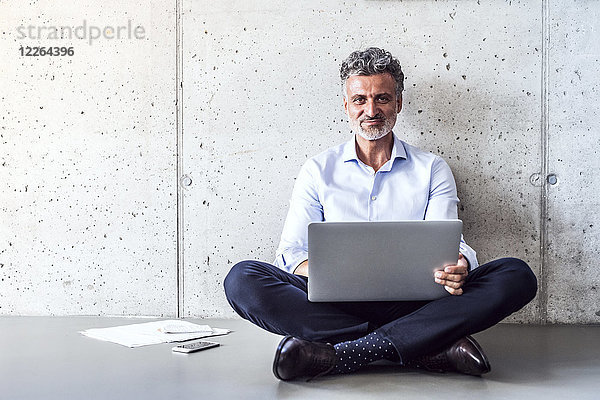 Porträt eines selbstbewussten  reifen Geschäftsmannes auf dem Boden sitzend mit Laptop