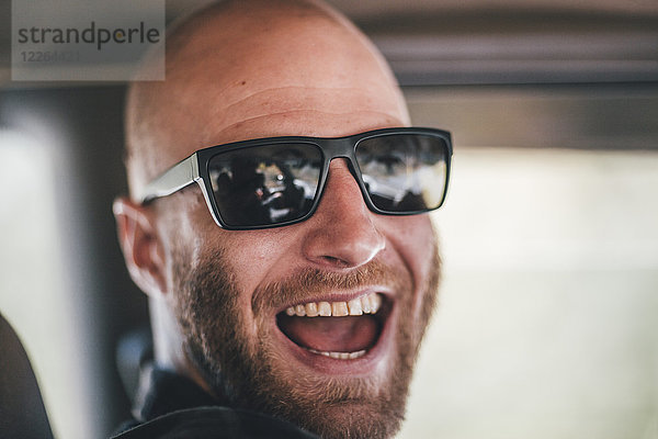 Porträt eines glücklichen jungen Mannes mit Sonnenbrille und Bart auf einem Roadtrip