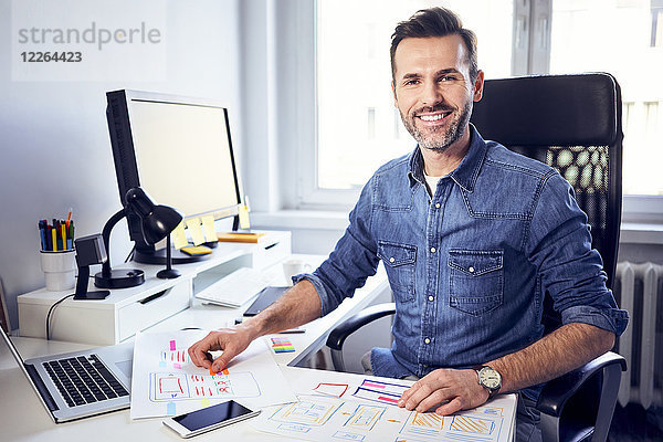 Porträt eines lächelnden Webdesigners bei der Arbeit am Schreibtisch im Büro