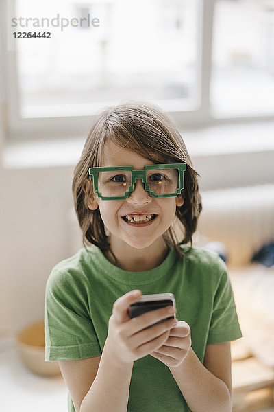 Porträt eines lächelnden Jungen mit einer Pixelbrille  der sein Handy hält.