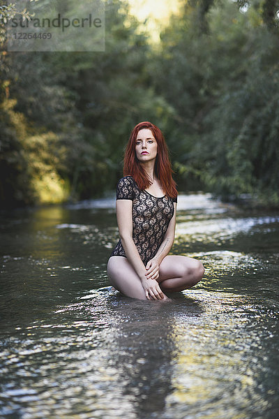 Porträt einer rothaarigen jungen Frau im transparenten schwarzen Body  die im Wasser hockt.