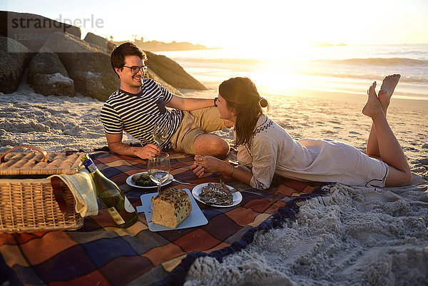 Glückliches Paar beim Picknick am Strand bei Sonnenuntergang
