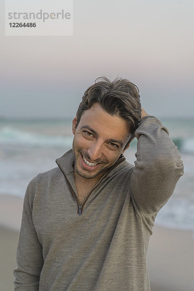 Porträt des lächelnden jungen Mannes am Strand bei Dämmerung