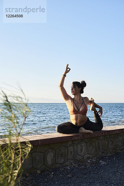 Junge Frau beim Yoga an einer Wand am Meer