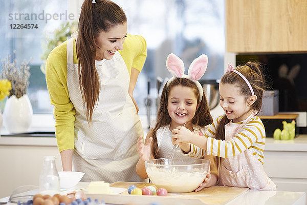 Glückliche Mutter und Töchter backen gemeinsam Osterkekse in der Küche
