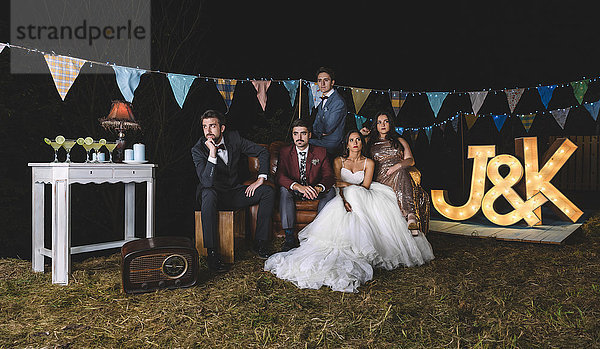 Porträt des Hochzeitspaares mit Freunden auf dem Sofa auf einer Nachtfeld-Party