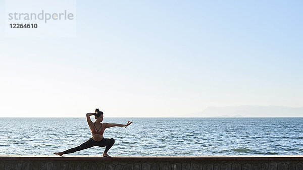 Junge Frau beim Yoga an einer Wand am Meer