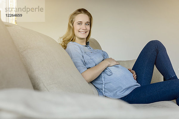 Porträt einer lächelnden Schwangeren  die zu Hause auf der Couch sitzt.
