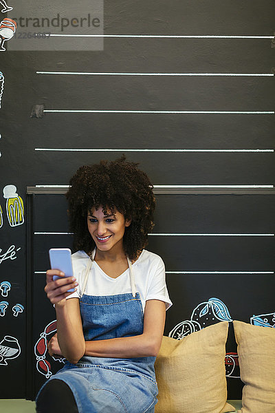 Lächelnde Frau sitzt auf einer Bank in einem Geschäft mit Handy