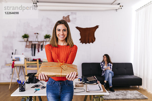 Lächelnde Modedesignerin hält eine verpackte Packung im Atelier