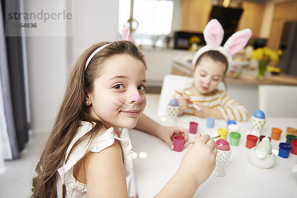 Porträt eines lächelnden Mädchens mit Schwester am Tisch sitzend Ostereier malend