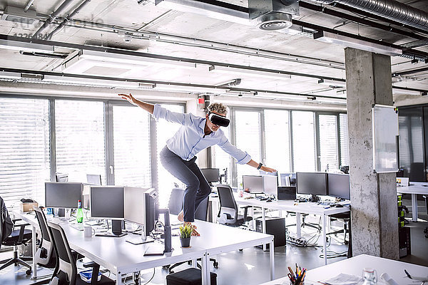 Barfuss reifer Geschäftsmann auf Schreibtisch im Büro mit VR-Brille