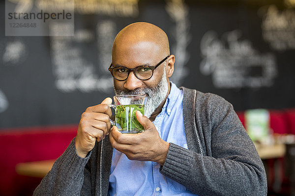 Porträt eines lächelnden Mannes mit einem Glas Tee im Café