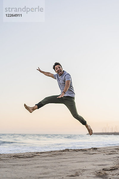 Glücklicher junger Mann  der bei Sonnenuntergang am Strand in die Luft springt.