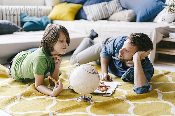 Vater und Sohn essen Pizza neben dem Globus auf dem Boden zu Hause
