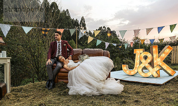 Braut auf dem Sofa liegend mit Bräutigam auf dem Feld