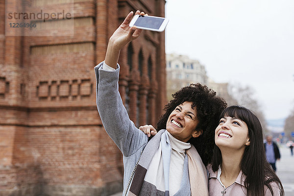 Spanien  Barcelona  zwei glückliche Frauen  die einen Selfie an einem Tor nehmen.