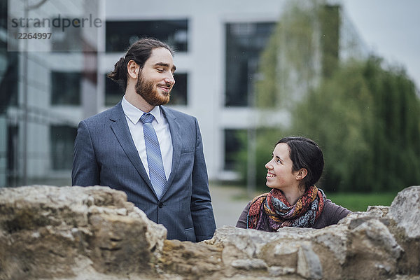 Lächelnder Geschäftsmann und Frau hinter einer Wand vor dem Bürogebäude
