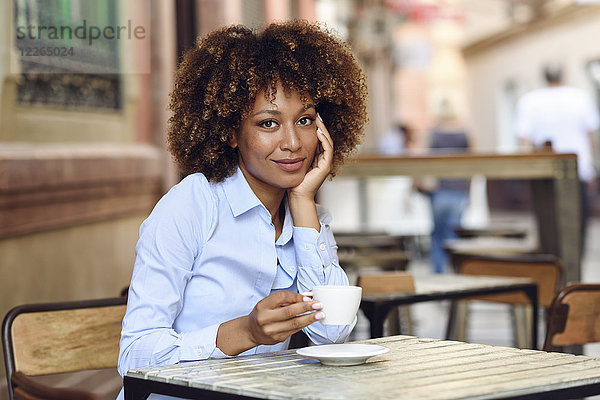 Porträt einer lächelnden Frau mit Afro-Frisur im Außencafé
