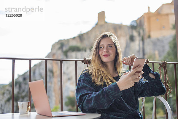 Spanien  Alquezar  Porträt einer entspannten jungen Frau mit Laptop und Handy auf der Terrasse