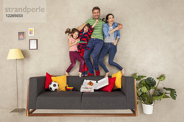 Glückliche Familie mit zwei Kindern beim Fußball schauen im Wohnzimmer