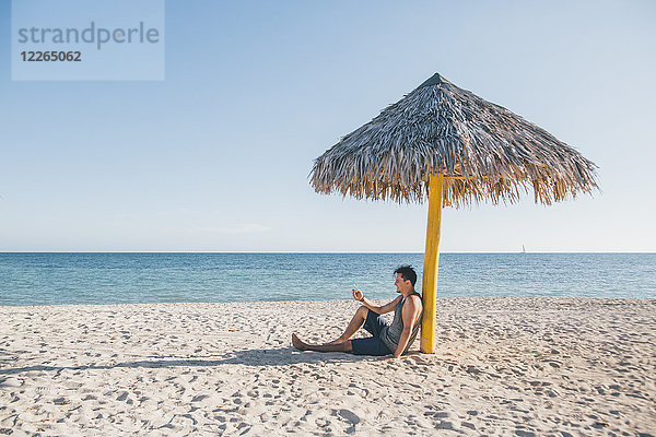 Kuba  Junger Mann sitzt unter einem Sonnenschirm am Playa Ancon