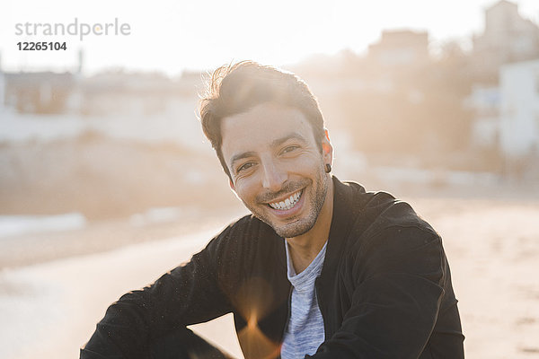 Porträt eines lächelnden jungen Mannes am Strand bei Sonnenuntergang