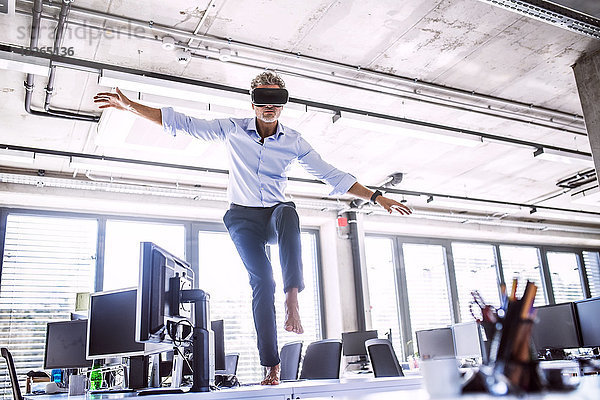 Barfuss reifer Geschäftsmann auf Schreibtisch im Büro mit VR-Brille
